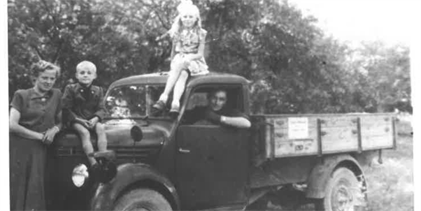 Ein altes schwarzweiß Foto von einem Lieferwagen mit der Familie Wildberger.